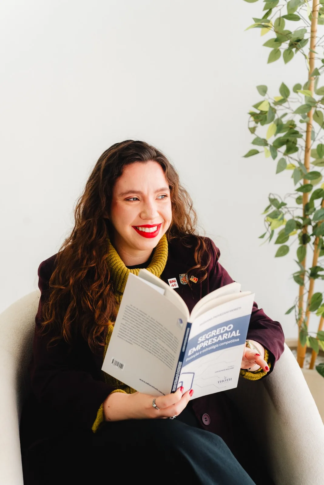 Ellen Landgraf sentada em uma poltrona, sorrindo, folheando o livro “Segredo empresarial: proteção e estratégia competitiva”.